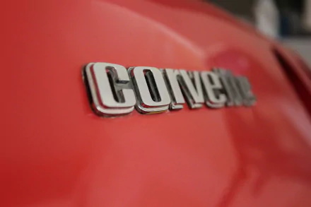 Close-up of the Chevrolet Corvette emblem on a vibrant red background, showcasing the iconic logo in a high-definition desktop wallpaper format.