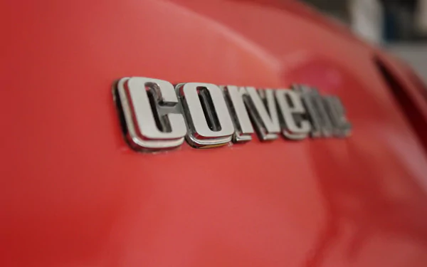 Close-up of the Chevrolet Corvette emblem on a vibrant red background, showcasing the iconic logo in a high-definition desktop wallpaper format.