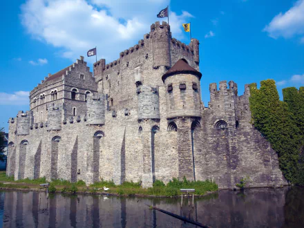 HD PC desktop wallpaper of Gravensteen, a medieval stone castle with fortified walls and towers under a bright blue sky.