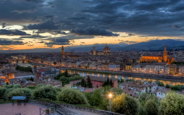 HD desktop wallpaper showcasing a stunning man-made cityscape of Florence at sunset, featuring illuminated historic buildings and the Arno River under a dramatic sky.