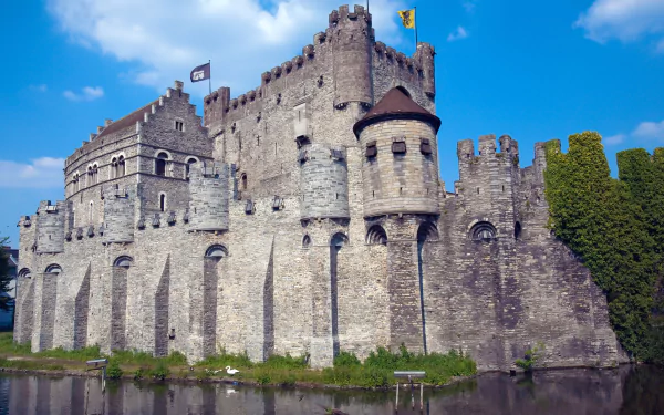 HD PC desktop wallpaper of Gravensteen, a medieval stone castle with fortified walls and towers under a bright blue sky.