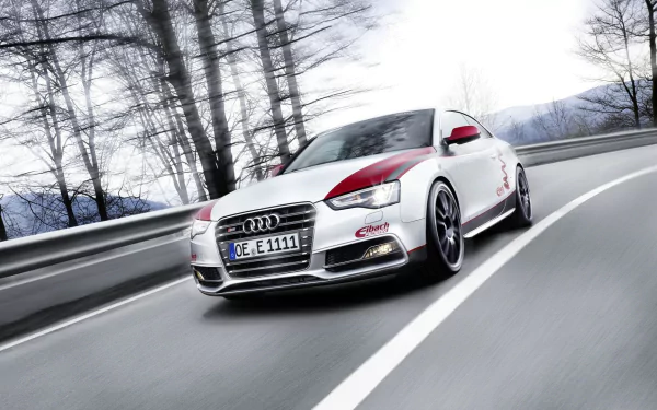 Dynamic low-angle shot of an Audi S5 vehicle speeding along a mountain road, rendered as a high-definition PC desktop wallpaper background.