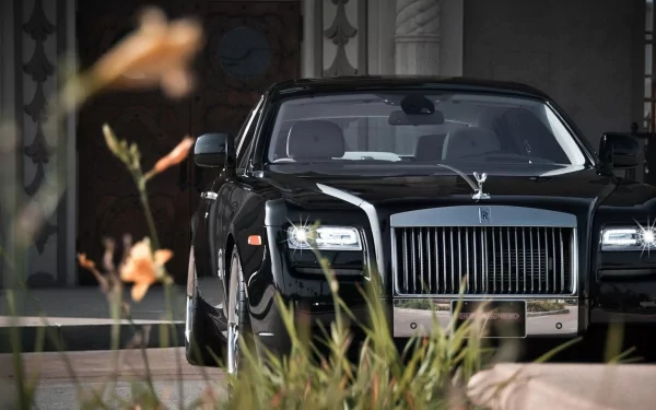 A sleek black Rolls-Royce Ghost positioned elegantly amidst soft foliage, showcasing luxury and sophistication in a stunning HD desktop wallpaper.