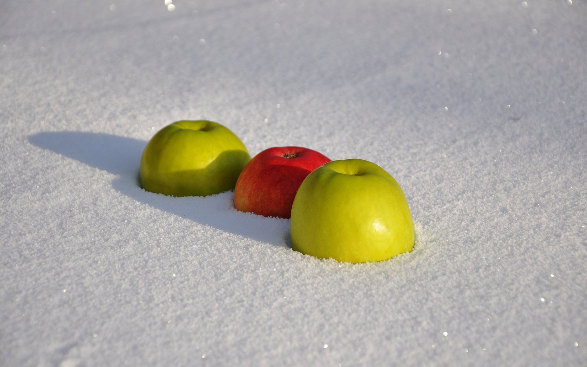 2K Quad HD PC desktop wallpaper: two green apples and one red apple half-submerged in sparkling snow, casting soft shadows.