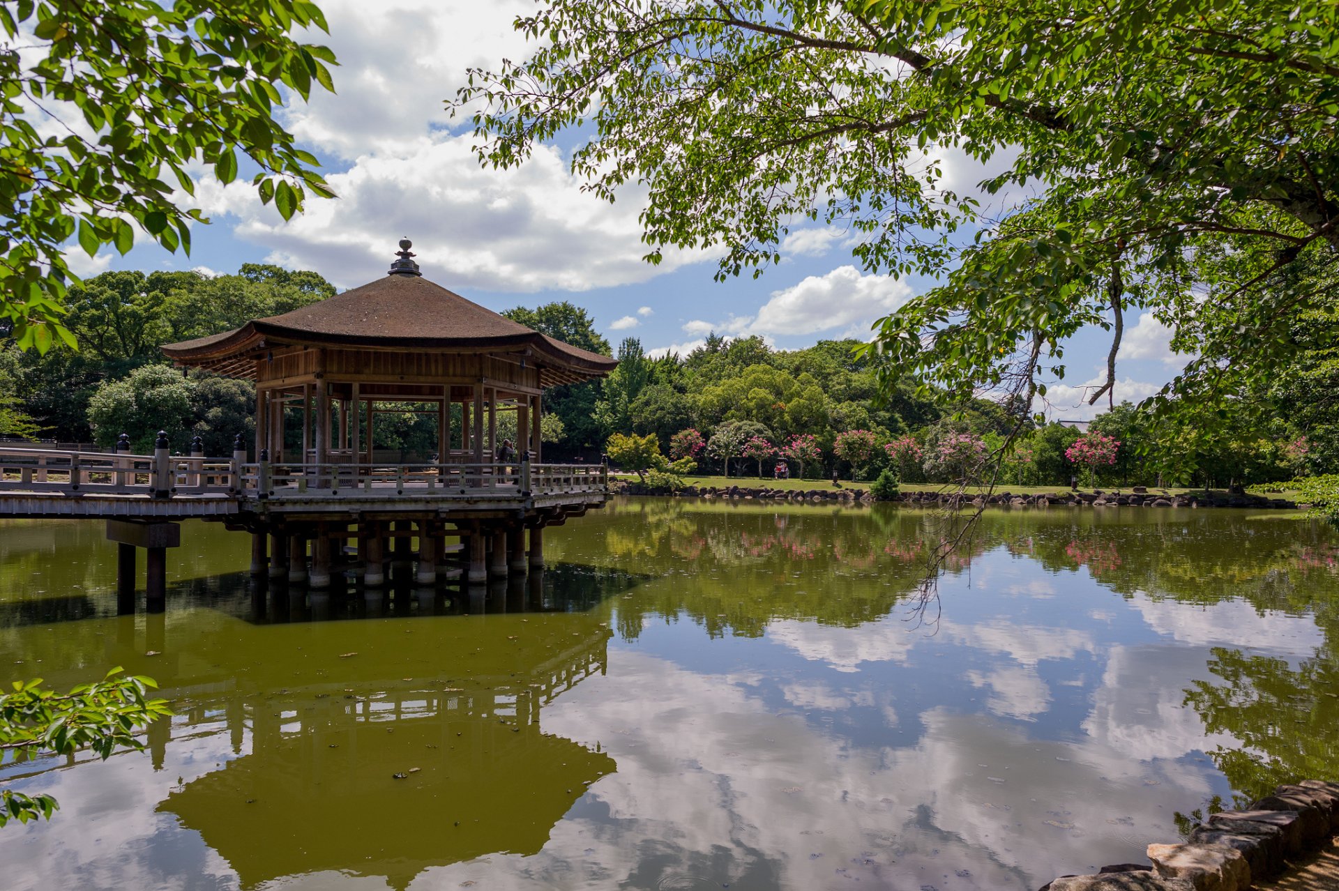 Scenic view of the Ukimido Pavilion gazebo reflecting on a tranquil pond, surrounded by lush trees in Nara Park, Japan, captured in a vibrant HD desktop wallpaper.