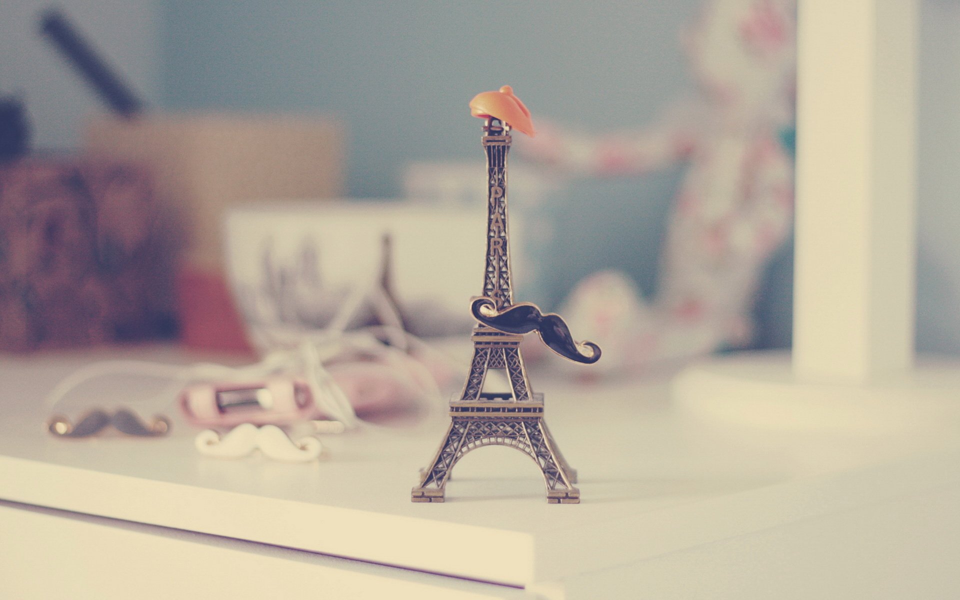 HD still life photography of a miniature Eiffel Tower figurine with a small hat and mustache, styled as a PC desktop wallpaper and background.