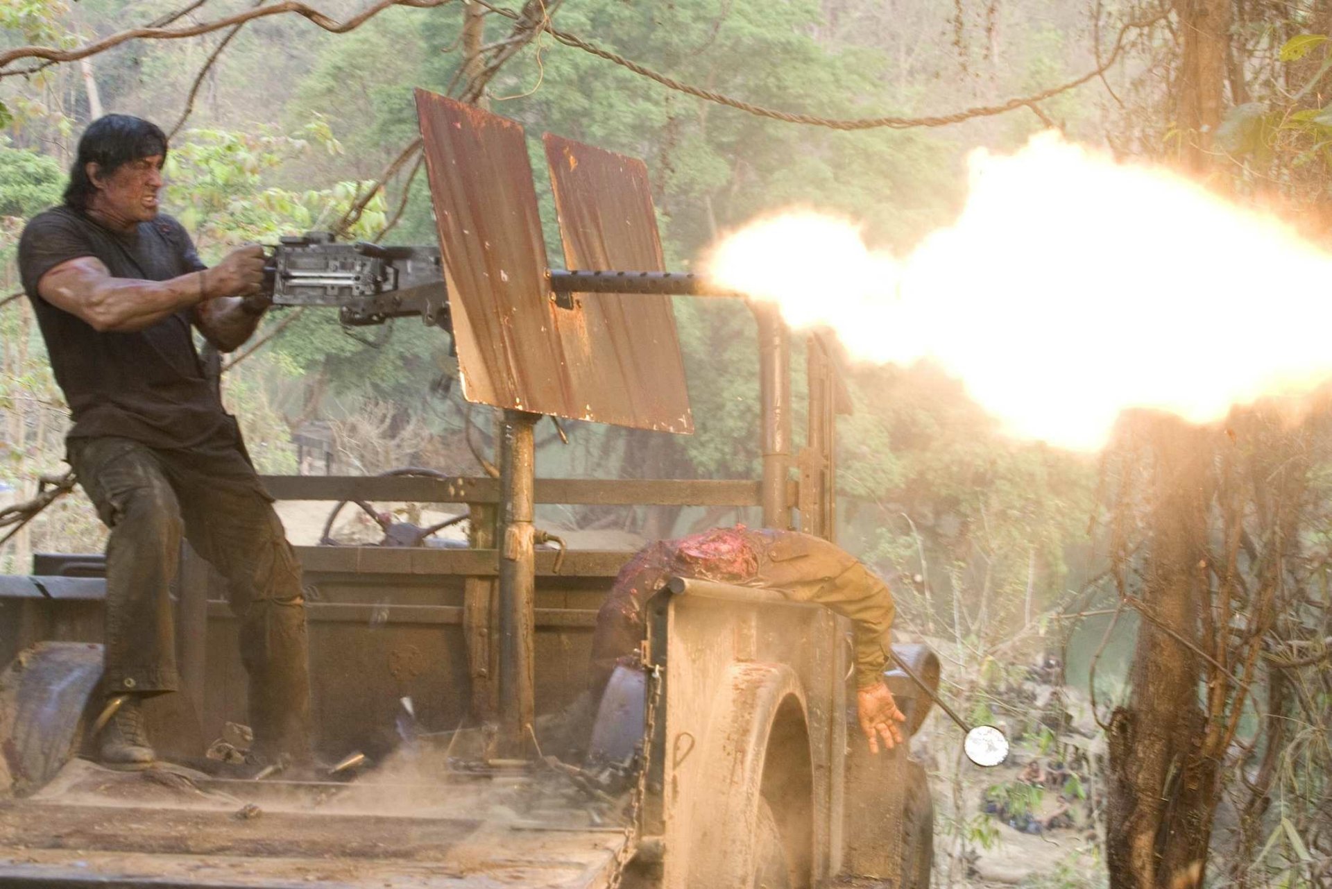 A high-definition wallpaper featuring a scene from the movie Rambo, depicting an intense action moment with the protagonist firing a heavy machine gun amidst a jungle setting.