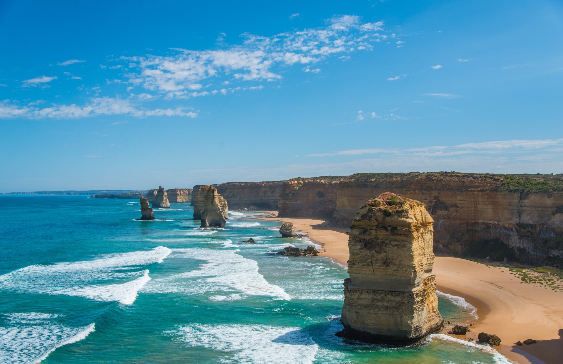 4K Ultra HD nature wallpaper showcasing a stunning coastline with towering rock formations, turquoise waves, and a clear blue sky.