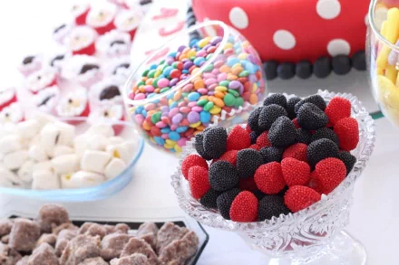 A colorful assortment of candies displayed in various bowls, featuring red and black gummy candies, vibrant chocolate-coated candies, and fluffy marshmallows, set against a cheerful background.