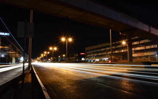 4K Ultra HD time-lapse photograph capturing streaks of light from moving vehicles on a city street at night, with illuminated streetlights and urban buildings.
