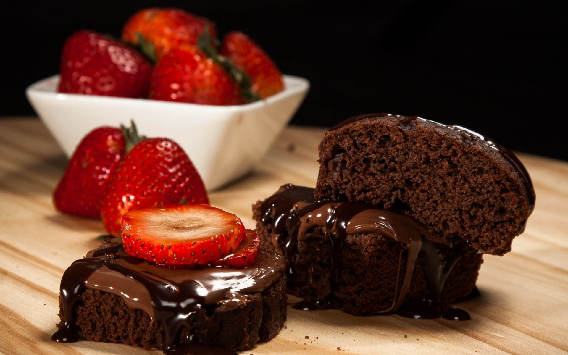 HD wallpaper featuring a decadent chocolate pastry cake topped with glossy chocolate sauce and served with fresh strawberries on a wooden table.