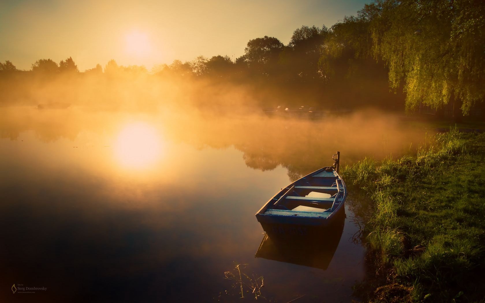 HD photography of a serene lake at sunrise with a small boat near the shore, surrounded by mist and lush greenery, captured as a PC desktop wallpaper and background.