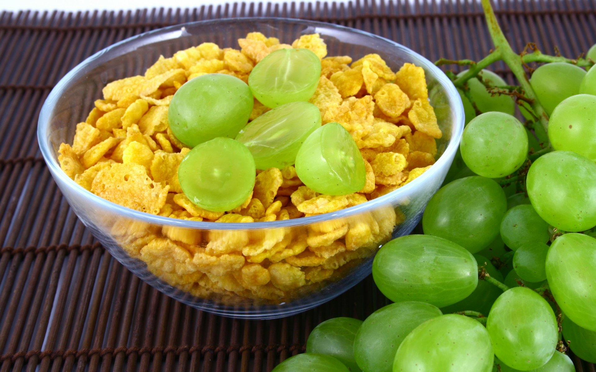 2K Quad HD PC wallpaper: glass bowl of cornflake cereal topped with halved green grapes, with a cluster of grapes beside it — food, cereal, fruit, breakfast.