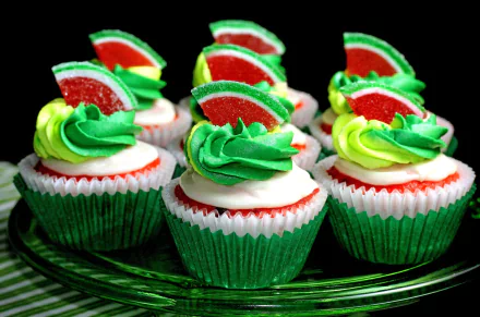HD wallpaper featuring vibrantly decorated cupcakes with green and white frosting, topped with red and green sugared gummy slices, presented on a glass plate.