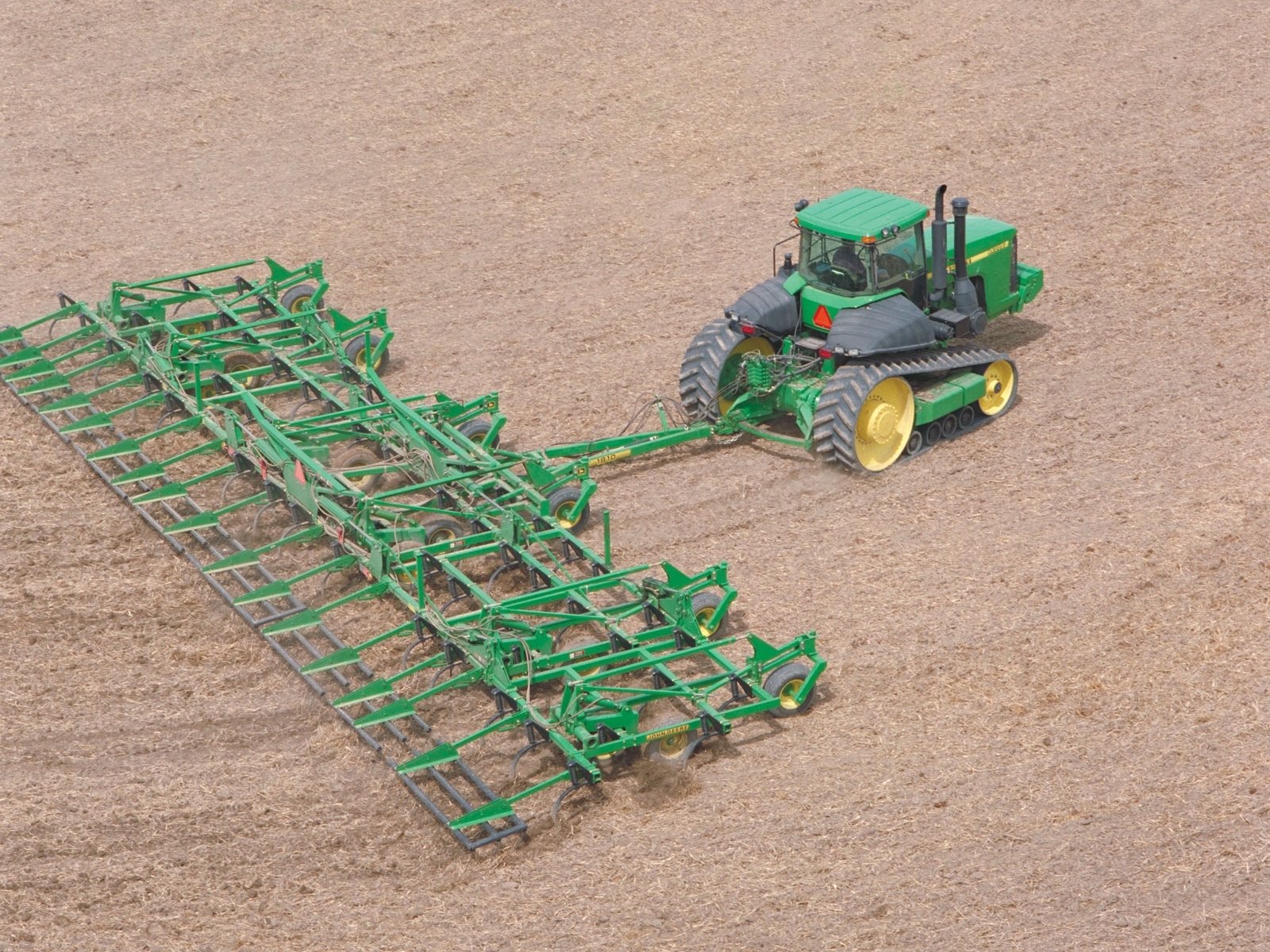 HD desktop wallpaper featuring a John Deere vehicle towing large green farming equipment across a plowed field.