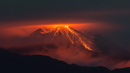 HD PC desktop wallpaper showing a glowing volcano erupting at night, with lava flowing and surrounded by dark clouds and mist in a dramatic natural scene.
