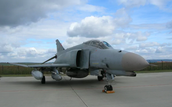 HD PC desktop wallpaper background showing a military McDonnell Douglas F-4 Phantom II parked on a tarmac under a cloudy sky.
