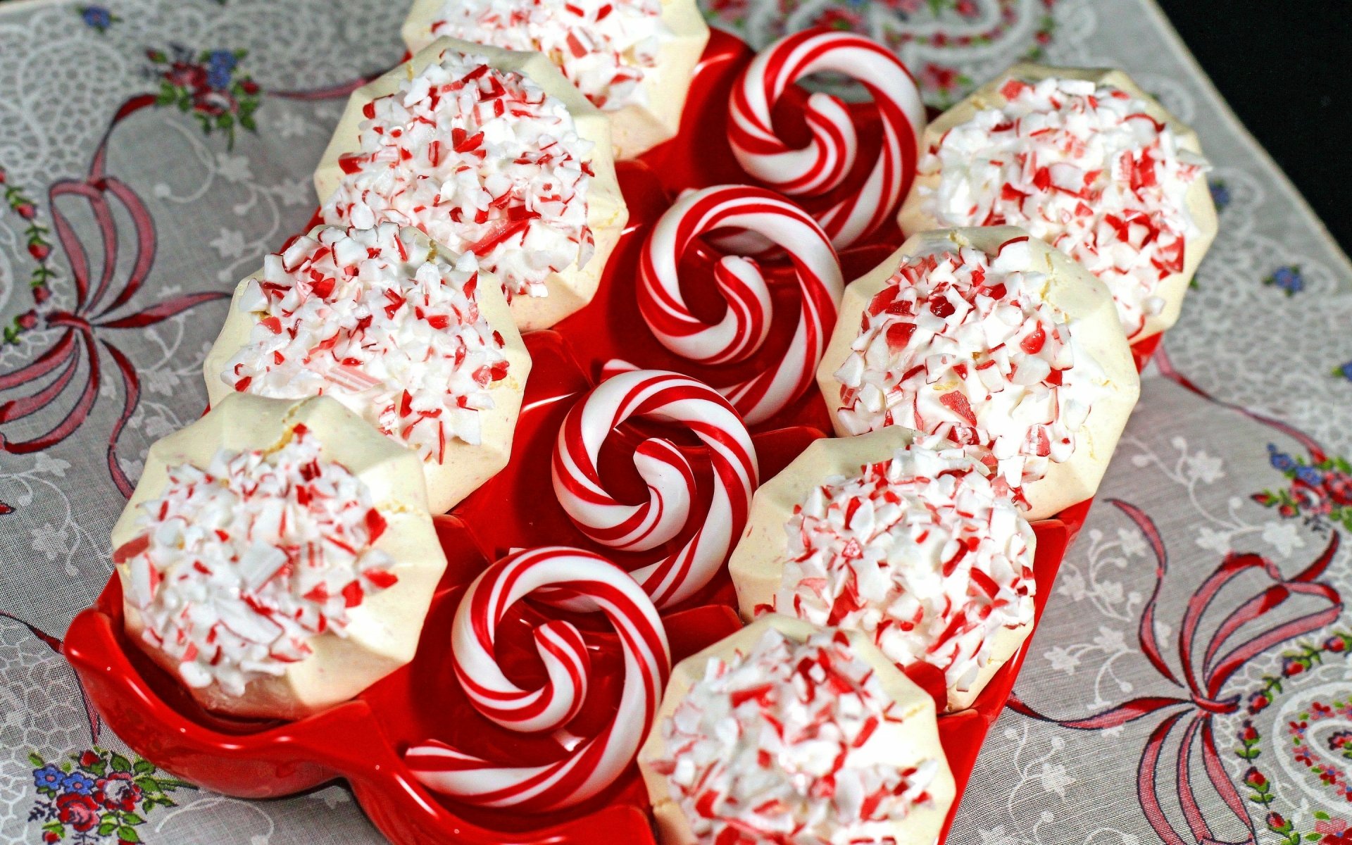 HD desktop wallpaper featuring a festive arrangement of peppermint swirl cookies and frosted cookies topped with crushed candy canes on a decorative tablecloth.