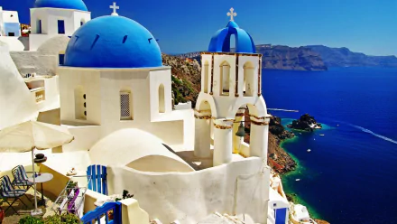 A breathtaking HD desktop wallpaper featuring a scenic view of a church with iconic blue domes, overlooking a stunning coastal landscape and clear blue waters.