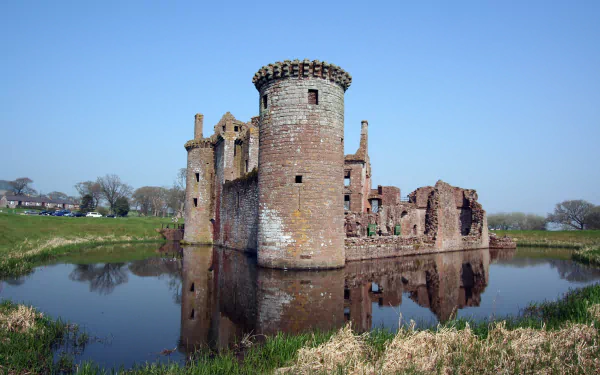 Caerlaverock Castle stands majestically by the water, showcasing its historic stone structure against a clear blue sky, making a striking HD desktop wallpaper and background.