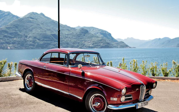 A classic red BMW 508 parked by a lakeside with mountains in the background, featured as a HD PC desktop wallpaper and background.
