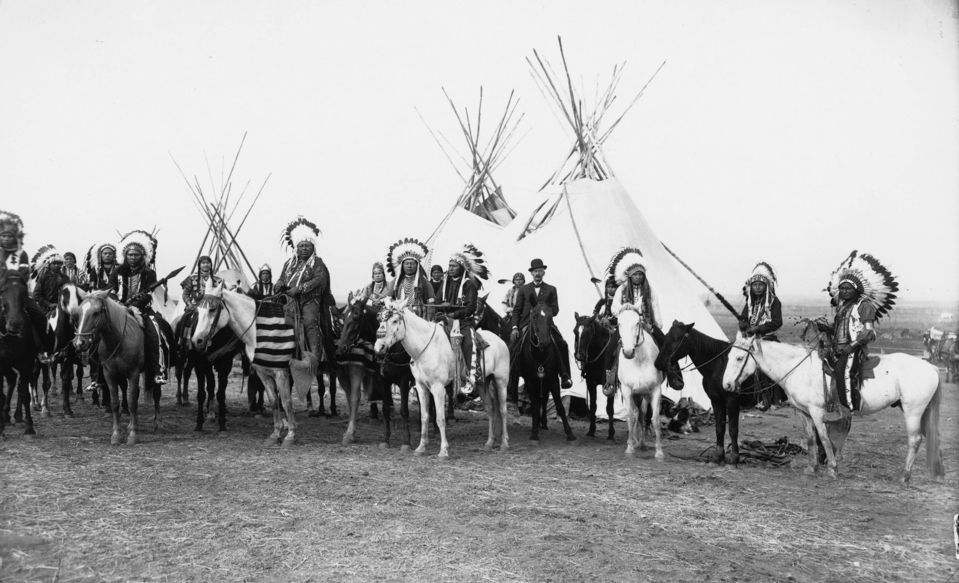 Black and white 4K Ultra HD photograph of Native American riders on horses standing in front of multiple tipis.