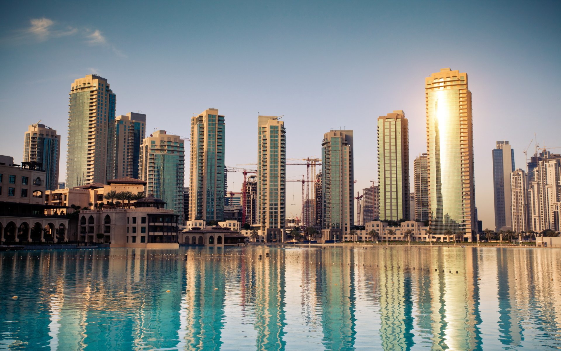 HD desktop wallpaper featuring a man-made skyline of Dubai with modern skyscrapers reflecting on calm water under a clear sky.
