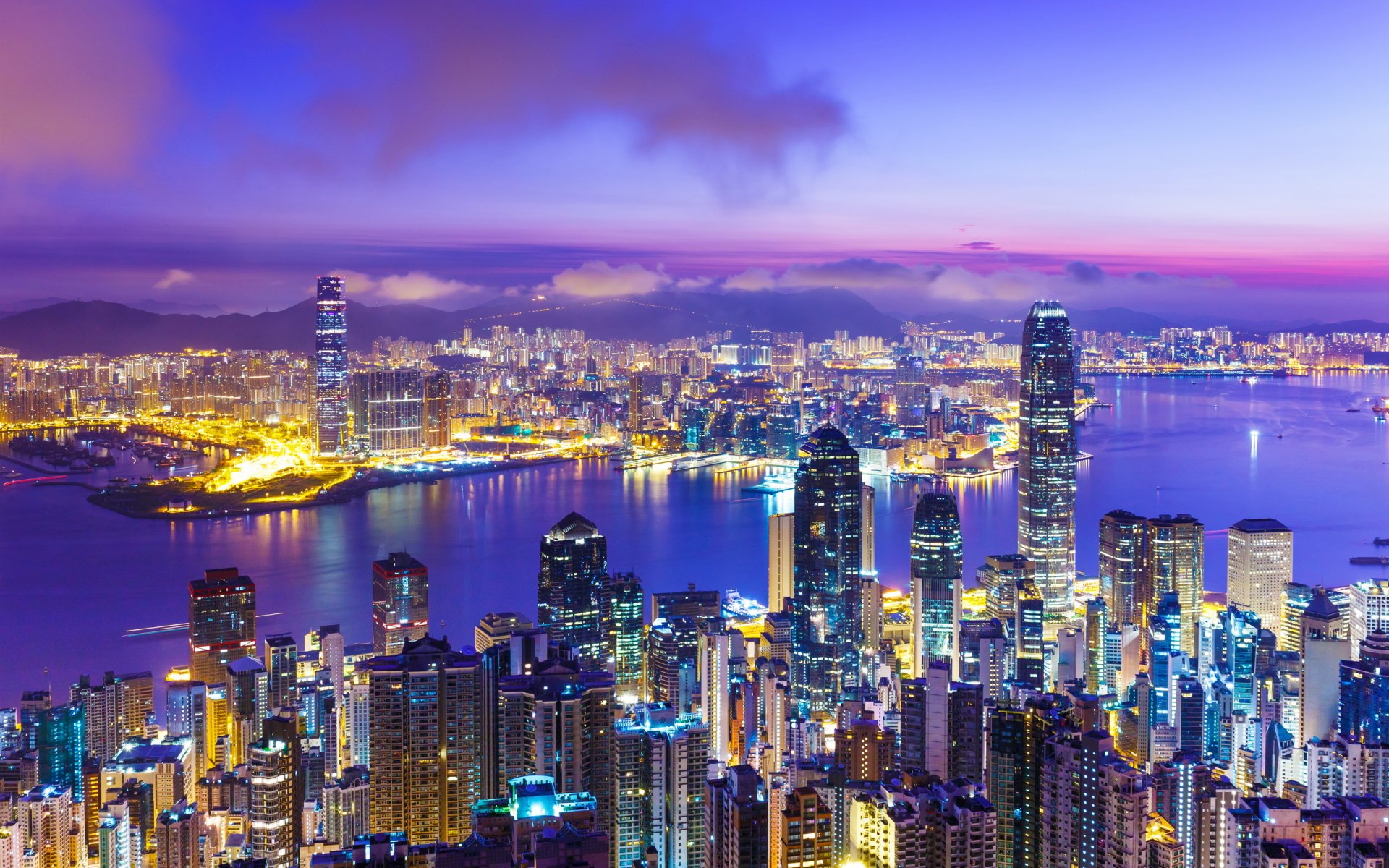 HD desktop wallpaper showcasing the vibrant man-made skyline of Hong Kong lit up against a twilight sky over the harbor.