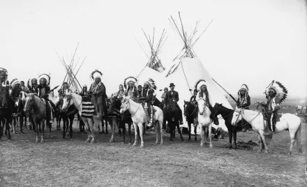 Black and white 4K Ultra HD photograph of Native American riders on horses standing in front of multiple tipis.