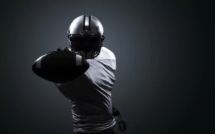 HD PC desktop wallpaper featuring a football player in full gear reaching out with the ball against a dark, minimalist background, emphasizing the intensity of the sport.