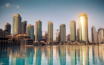 HD desktop wallpaper featuring a man-made skyline of Dubai with modern skyscrapers reflecting on calm water under a clear sky.