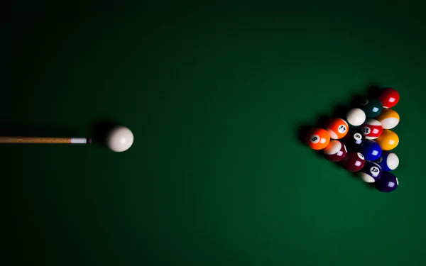 A close-up view of a pool table featuring a cue ball and a triangle arrangement of colorful billiard balls on a rich green felt background.