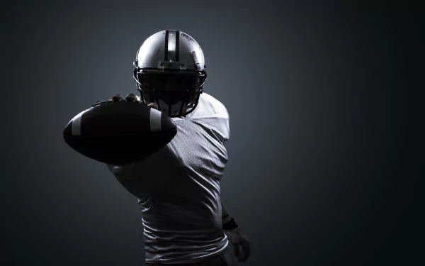 HD PC desktop wallpaper featuring a football player in full gear reaching out with the ball against a dark, minimalist background, emphasizing the intensity of the sport.