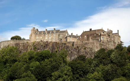 HD desktop wallpaper showcasing Stirling Castle, a historic man-made fortress perched atop a rocky hill surrounded by lush greenery under a clear blue sky.