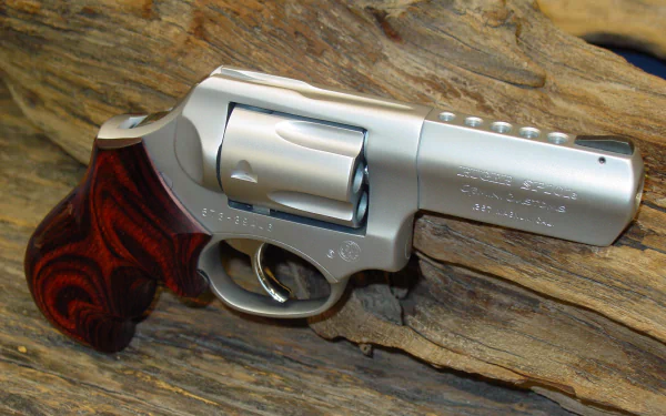 Close-up HD PC desktop wallpaper of a man-made Ruger stainless-steel revolver with wood grip resting on a textured wood background.