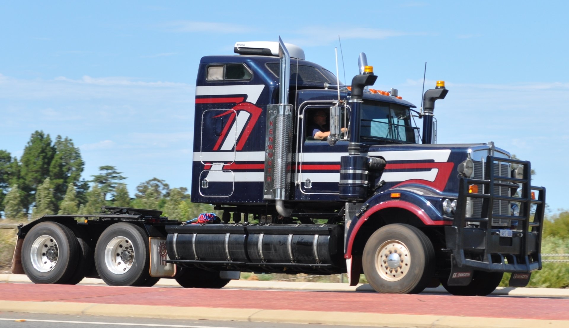 Blue Kenworth semi truck with red-white striping parked on a road, presented as a 2K Quad HD PC desktop wallpaper background.