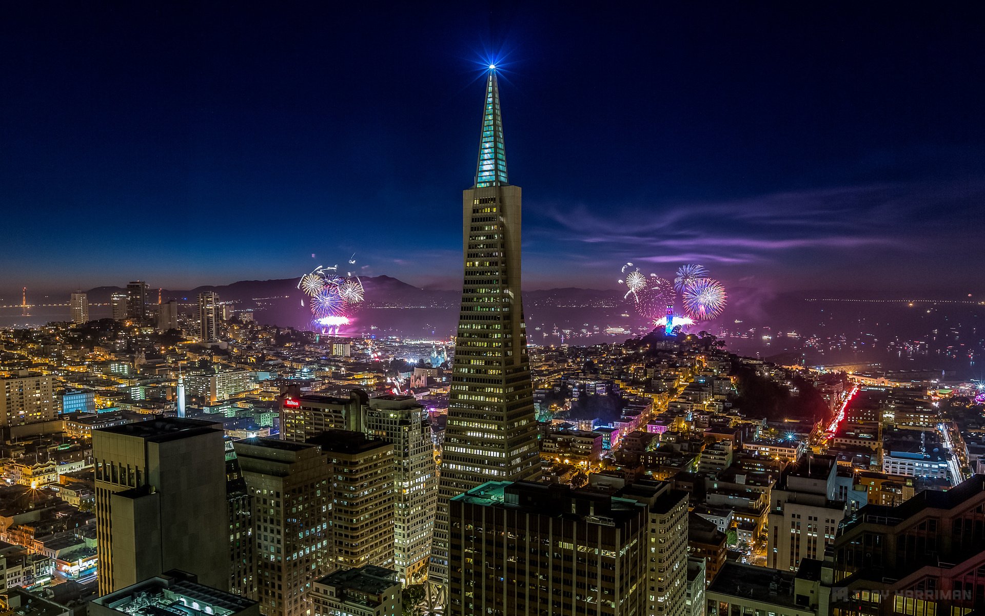 HD desktop wallpaper of San Francisco's cityscape at night, featuring the illuminated Transamerica Pyramid and fireworks lighting up the sky.