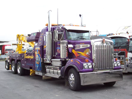 HD desktop wallpaper featuring a purple Kenworth tow truck with detailed graphics, parked among other trucks in a lot.