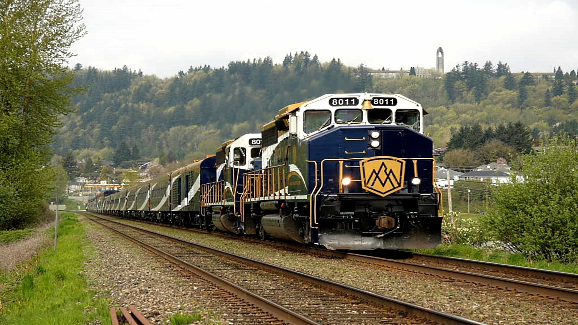 A powerful train navigates along tracks, flanked by lush greenery and distant hills, creating a striking scene for a HD PC desktop wallpaper and background.
