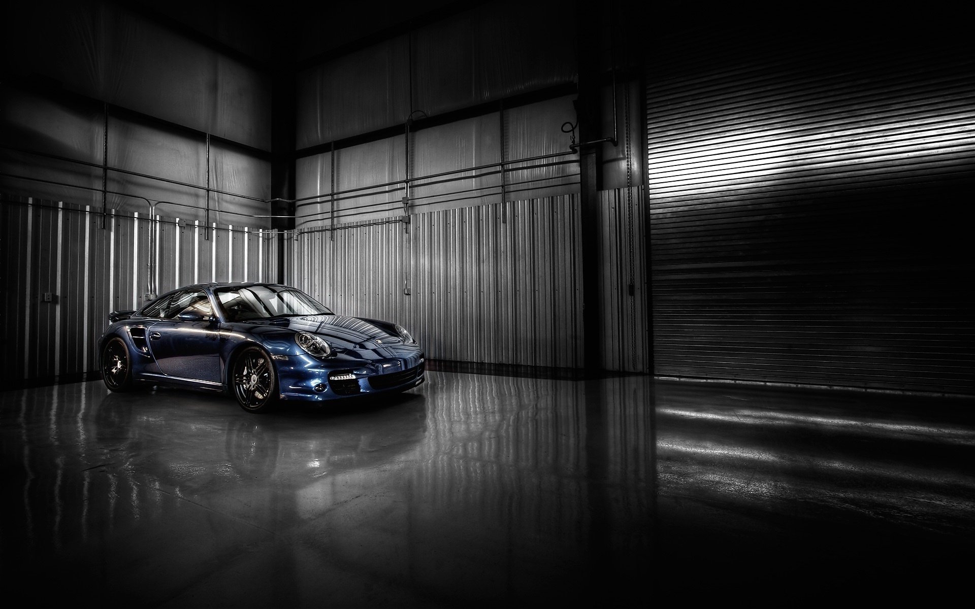 Sleek blue Porsche sports car parked in a dim industrial garage with glossy floor reflections — HD PC desktop wallpaper and background.