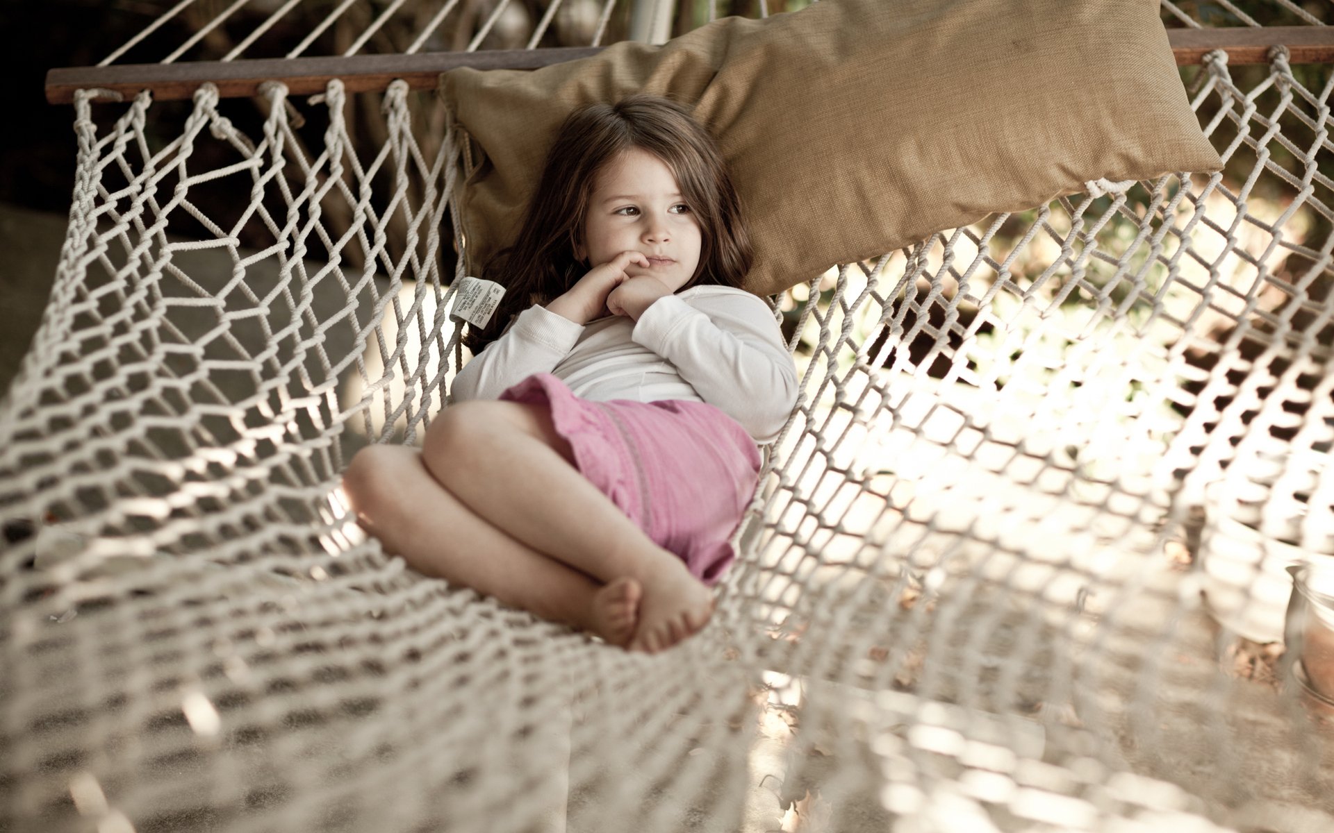 A child relaxes thoughtfully on a hammock, capturing a serene moment in a natural setting. This HD wallpaper adds a warm and whimsical touch to your desktop background.