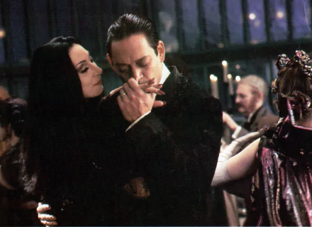 A scene from *The Addams Family* (1991), featuring Morticia and Gomez Addams sharing a romantic moment at a lavish gathering, set in a dark, atmospheric environment. Discover this 4K Ultra HD wallpaper.