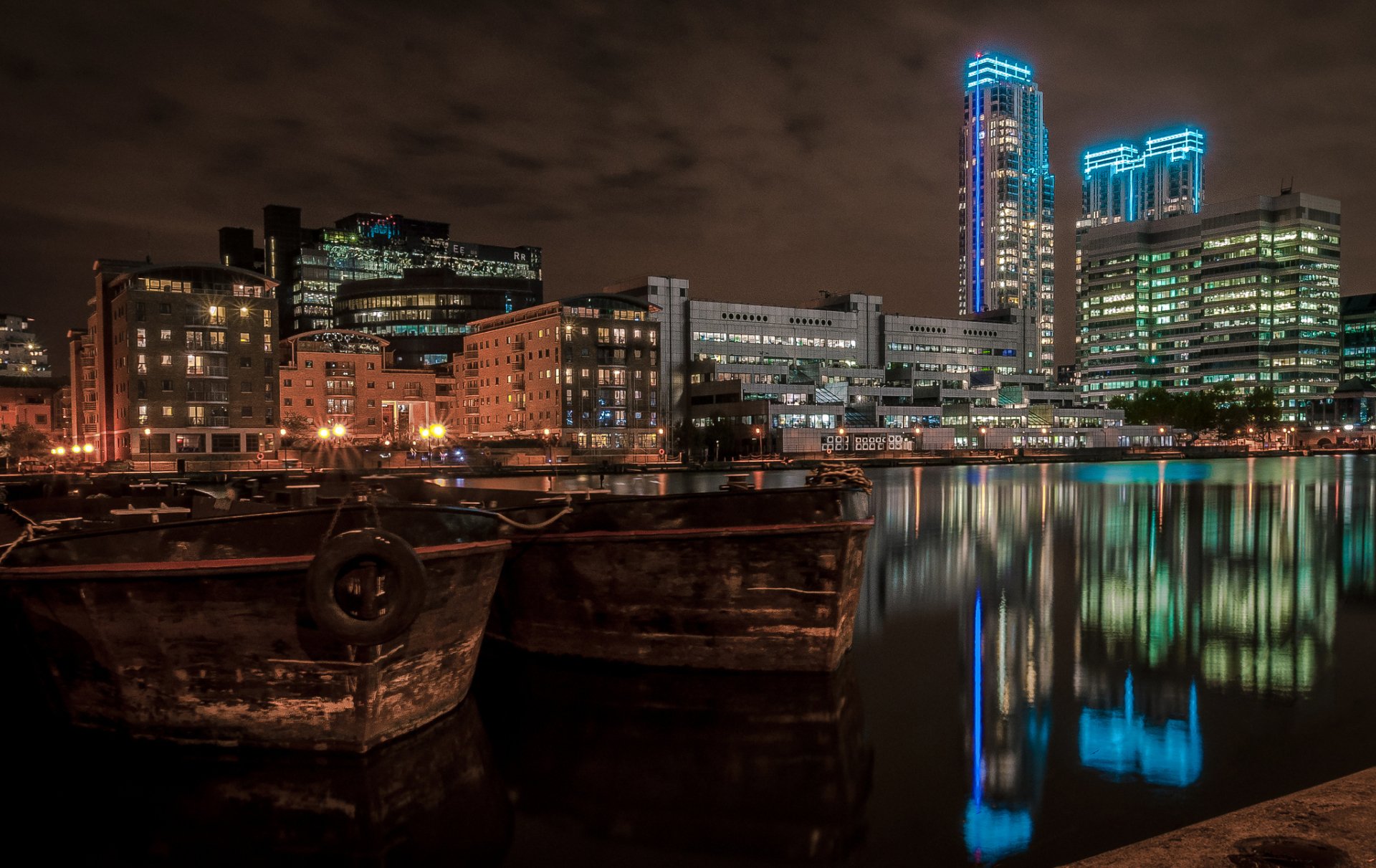Nighttime view of man-made London waterfront with illuminated modern buildings reflecting on calm water, captured as an HD PC desktop wallpaper and background.