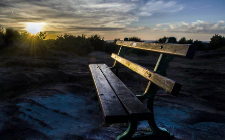 A scenic view of a wooden bench at sunset, surrounded by trees and clouds, creating a tranquil atmosphere. This HD image serves as a beautiful desktop wallpaper and background.