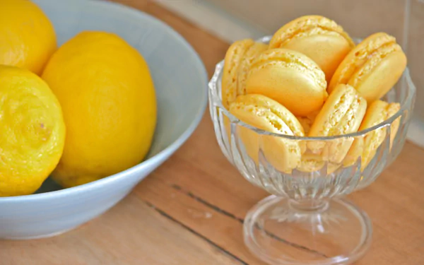 A 4K Ultra HD desktop wallpaper featuring yellow macarons in a glass dish next to a bowl of fresh lemons on a wooden surface.