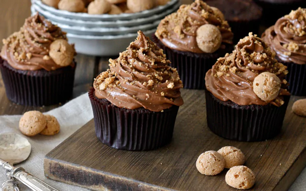 HD desktop wallpaper featuring rich chocolate cupcakes topped with creamy frosting and decorated with small cookies, set on a wooden table.
