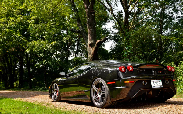 HD PC desktop wallpaper featuring a sleek black Ferrari 430 Scuderia parked on a gravel path surrounded by lush green trees in natural daylight.