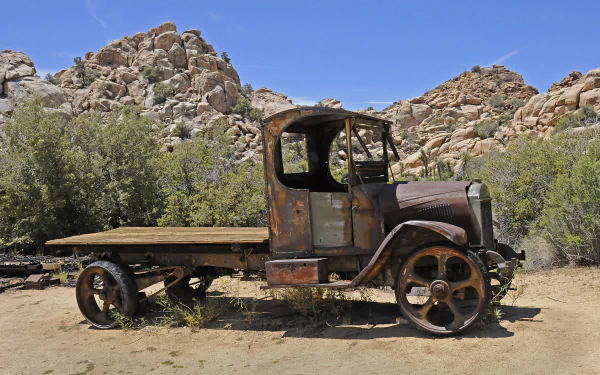 An old, weathered truck sits in a desert landscape, surrounded by rocky hills and sparse greenery. This HD wallpaper showcases a unique vehicle against a vibrant blue sky.