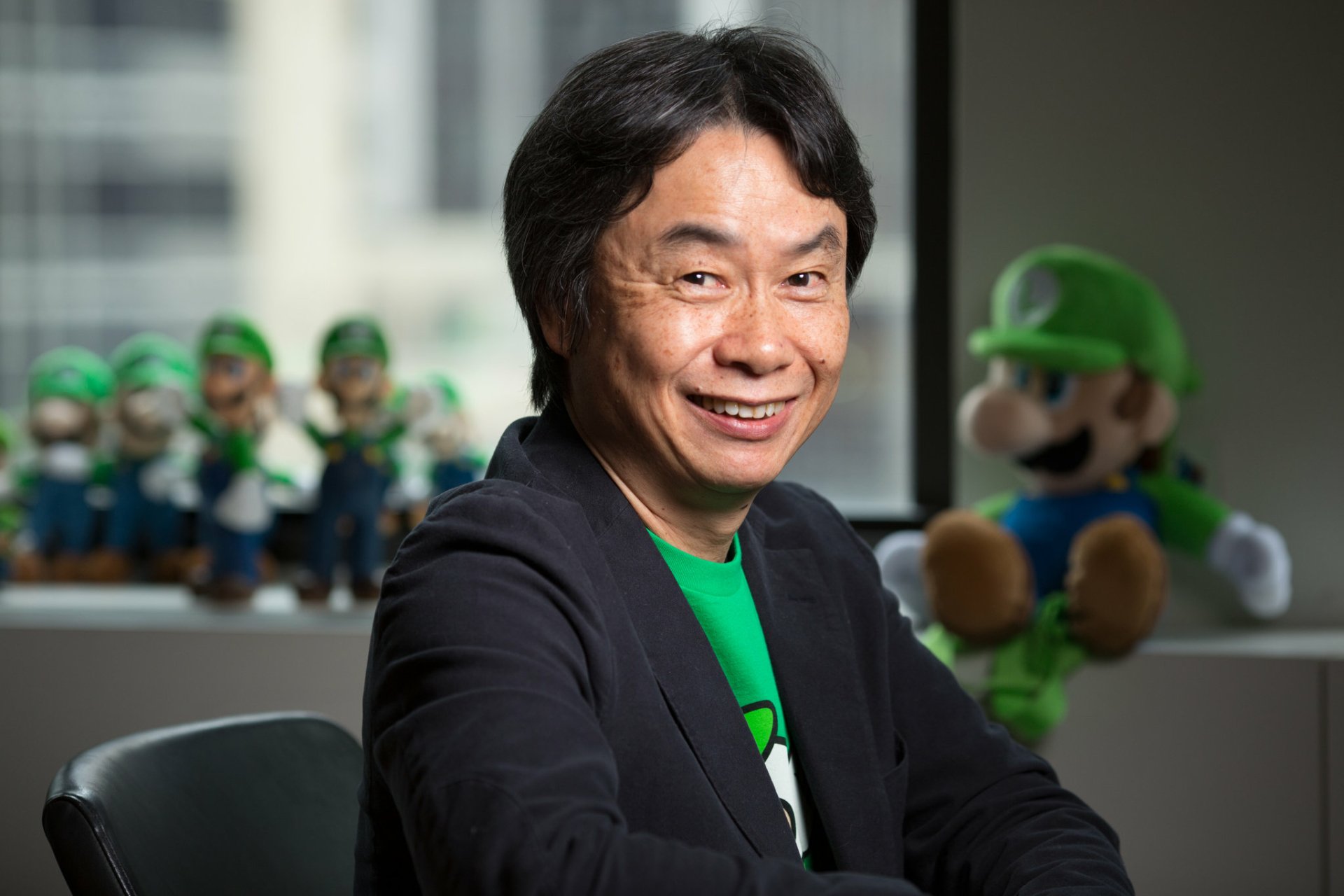 HD desktop wallpaper featuring a smiling person with a collection of Luigi figurines and a plush in the background.