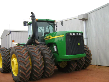A John Deere tractor with large tires is positioned in front of a building, showcasing its robust design, featured as a high-definition desktop wallpaper and background.
